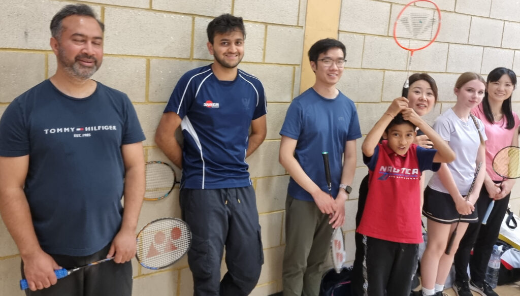 Diverse group enjoying indoor badminton session, smiling with rackets and sports attire.