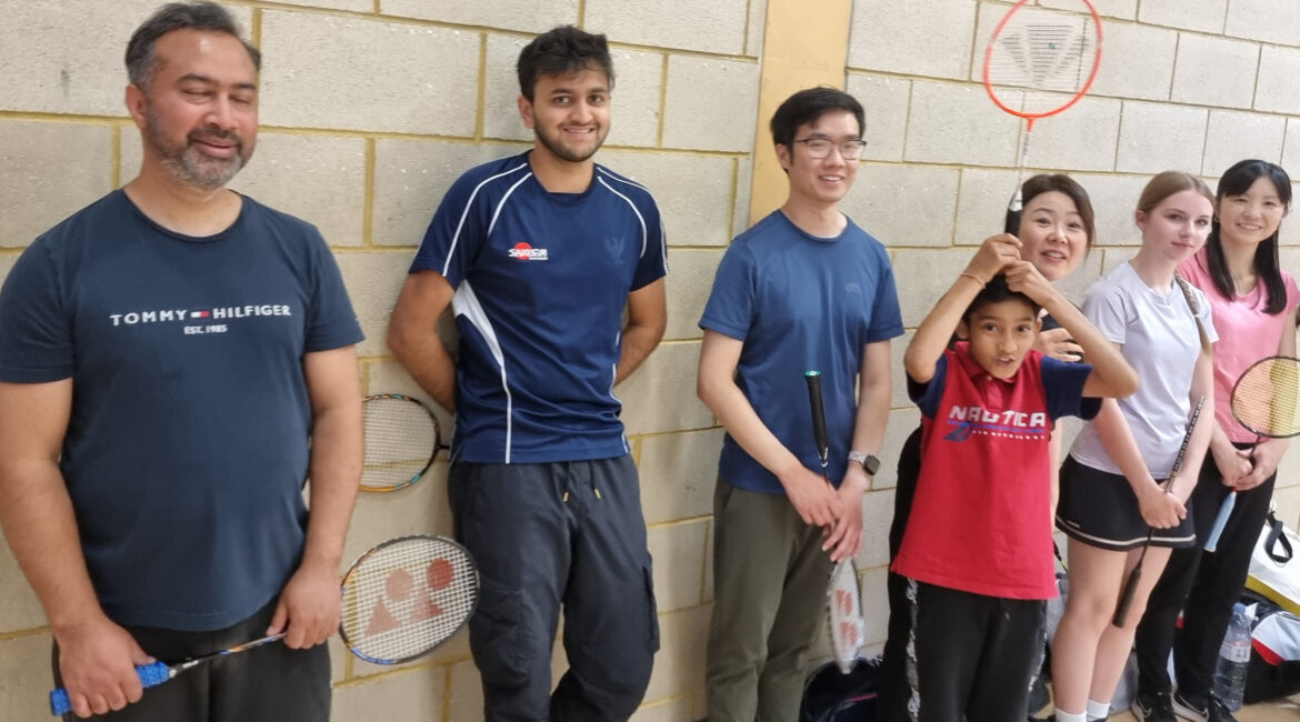 Diverse group enjoying indoor badminton session, smiling with rackets and sports attire.