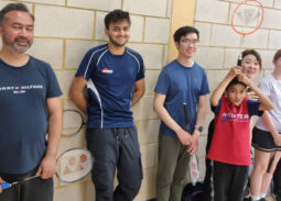 Diverse group enjoying indoor badminton session, smiling with rackets and sports attire.